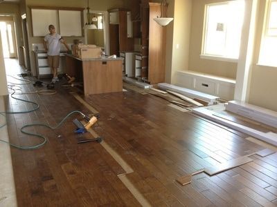 Kitchen and living area mid-renovation with dark wood flooring tools and person installing planks