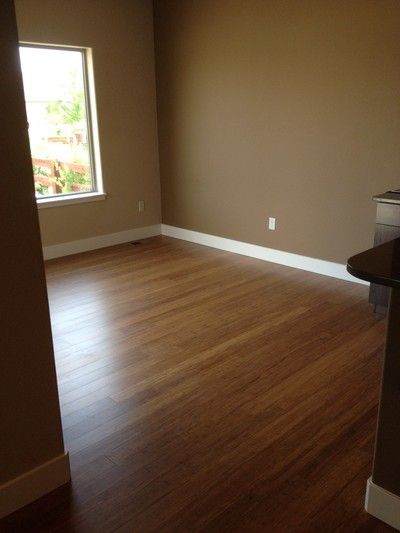 Empty room with brown walls, wood floors, single window, and white baseboards