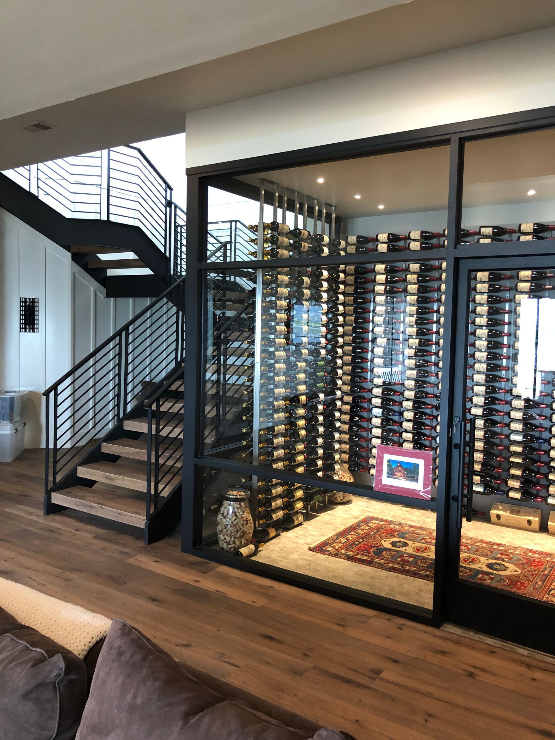 Glass wine cellar with metal racks beside wood staircase and cozy living space