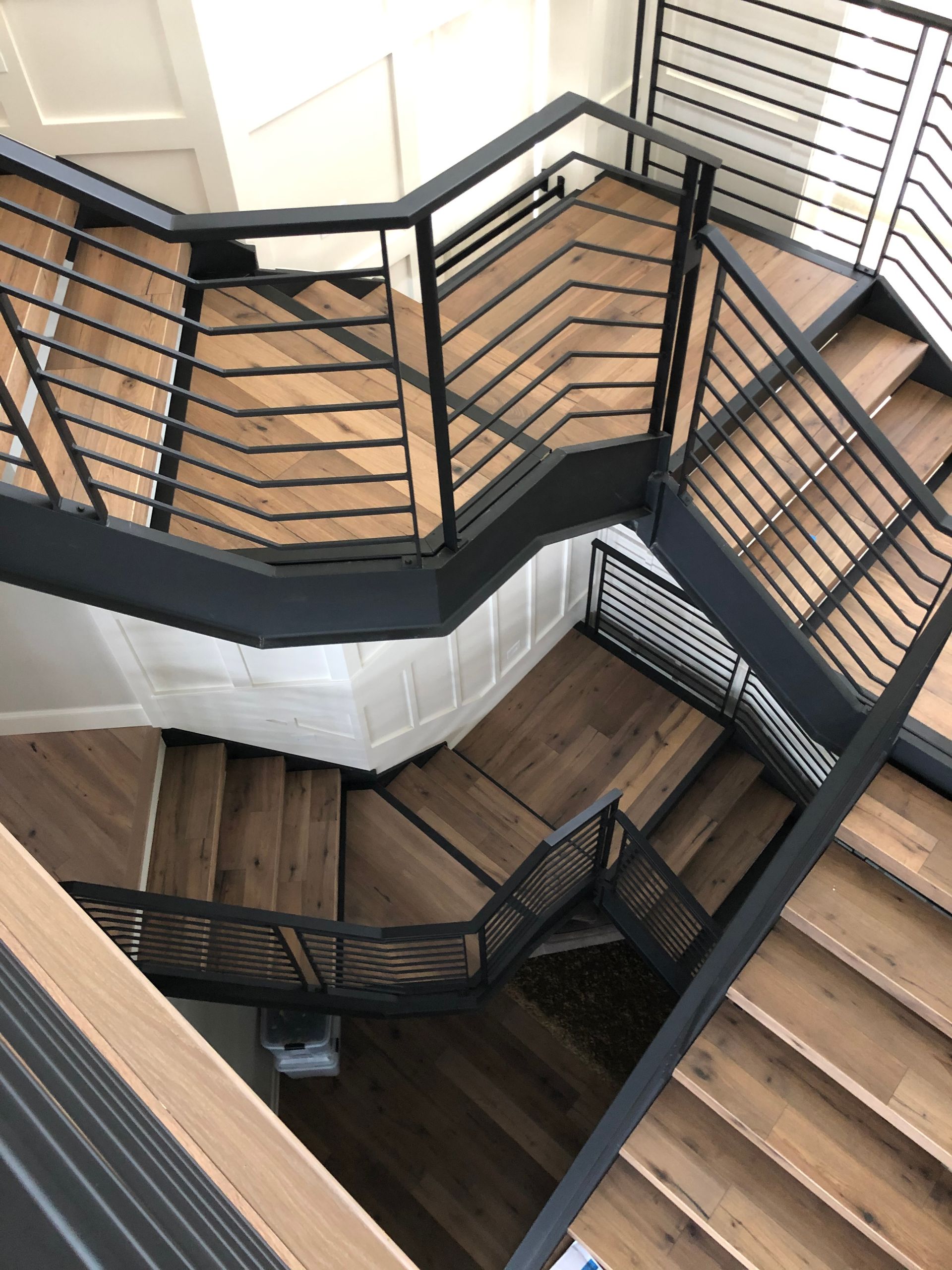 Zigzag staircase with wood steps, black horizontal railings, and paneled white walls