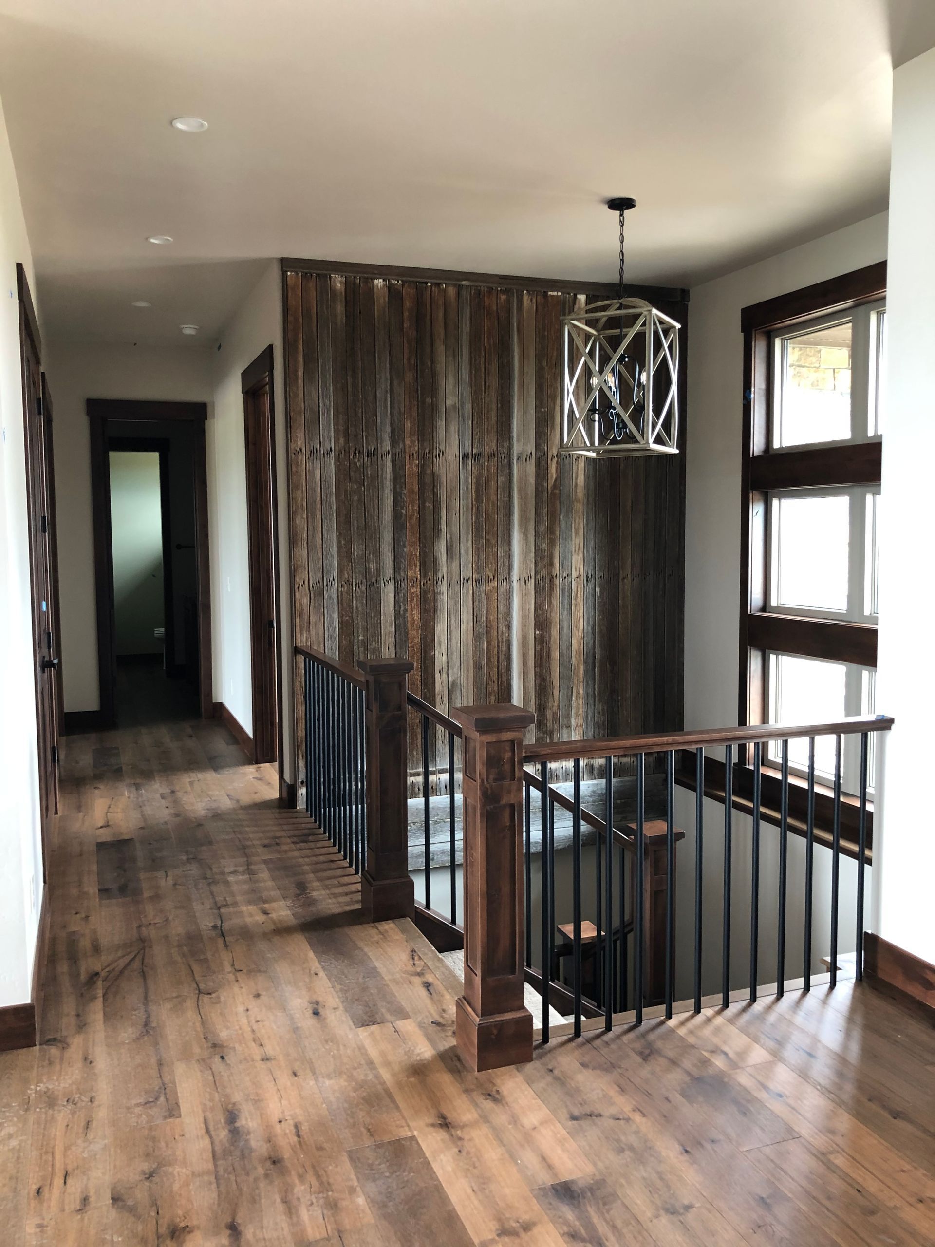 Rustic hallway with wood floors, accent wall, and staircase with black metal railing