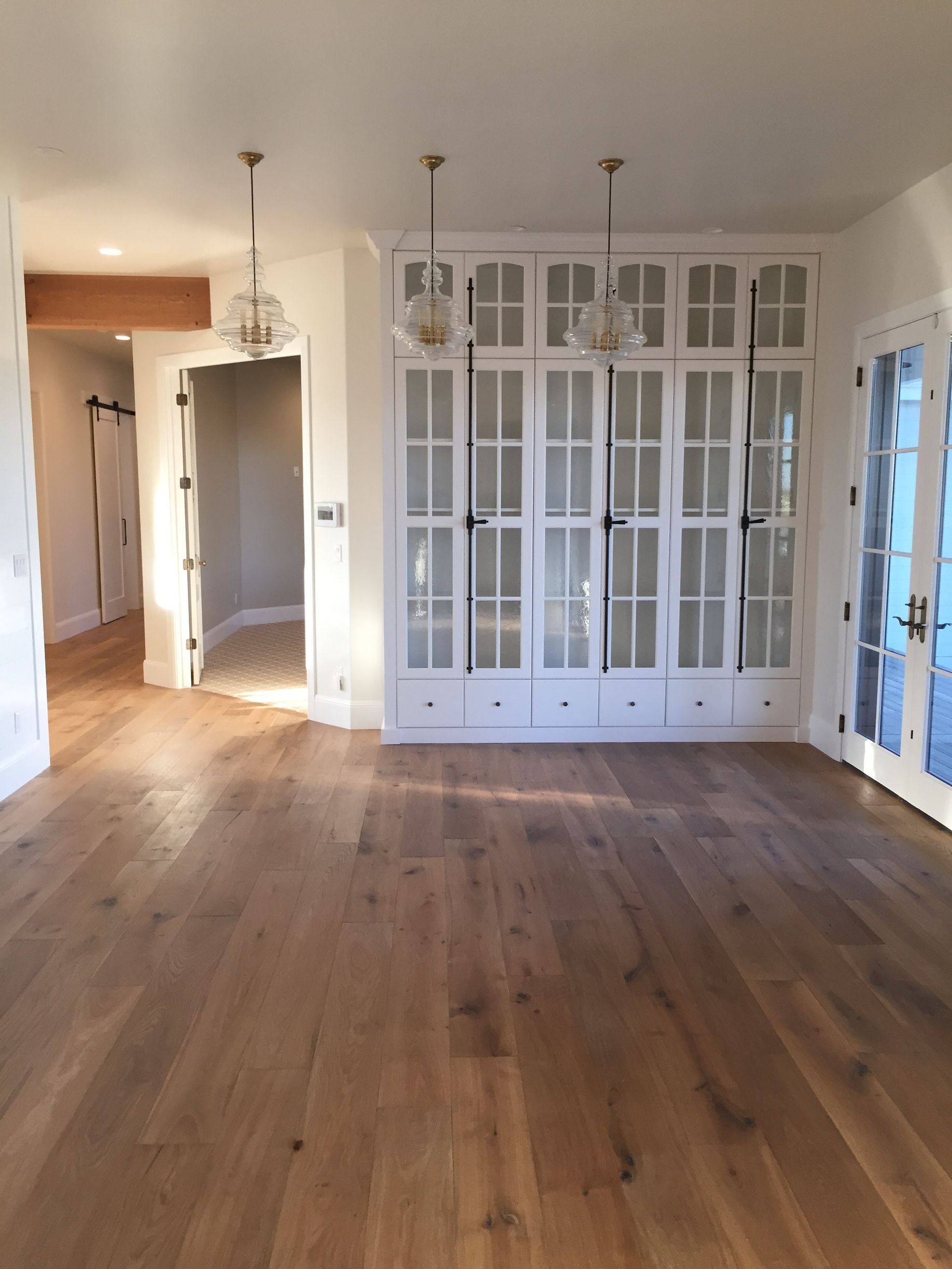 Built-in white cabinetry with glass doors, pendant lights, and wood flooring