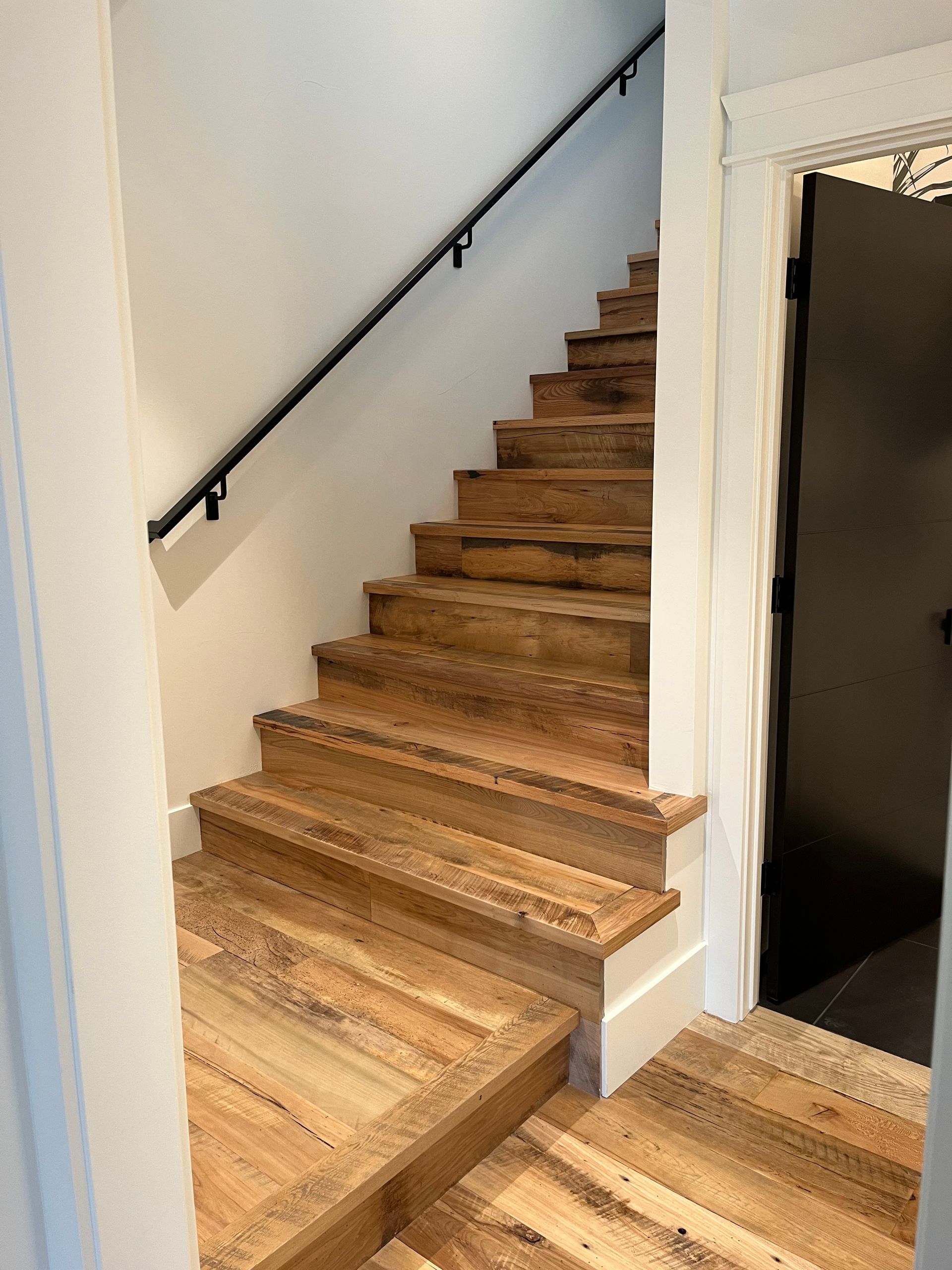 Wood staircase with black handrail beside white wall and open black doorway