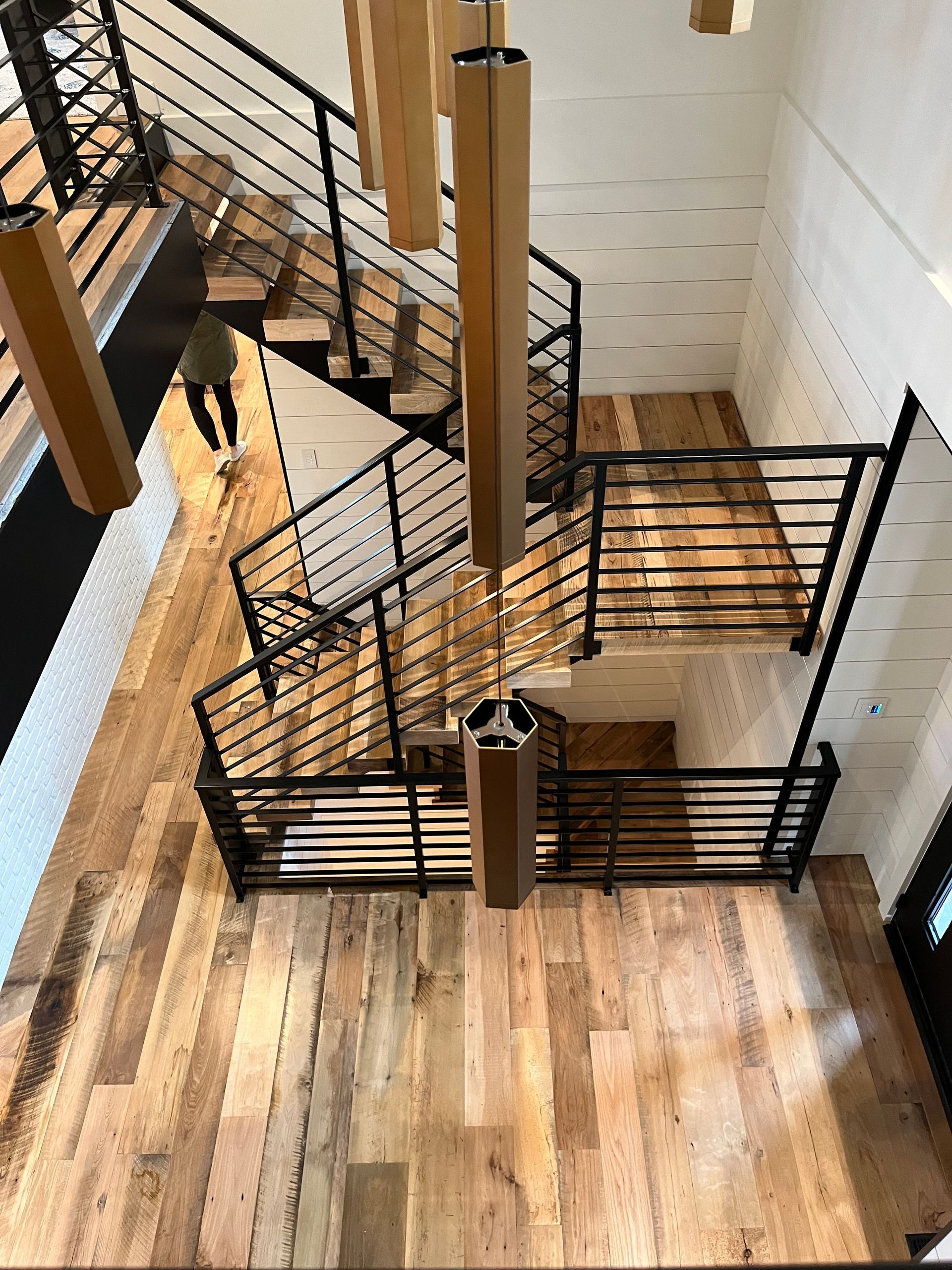 Multi-level staircase with black railings, wood floors, and hexagonal pendant lights