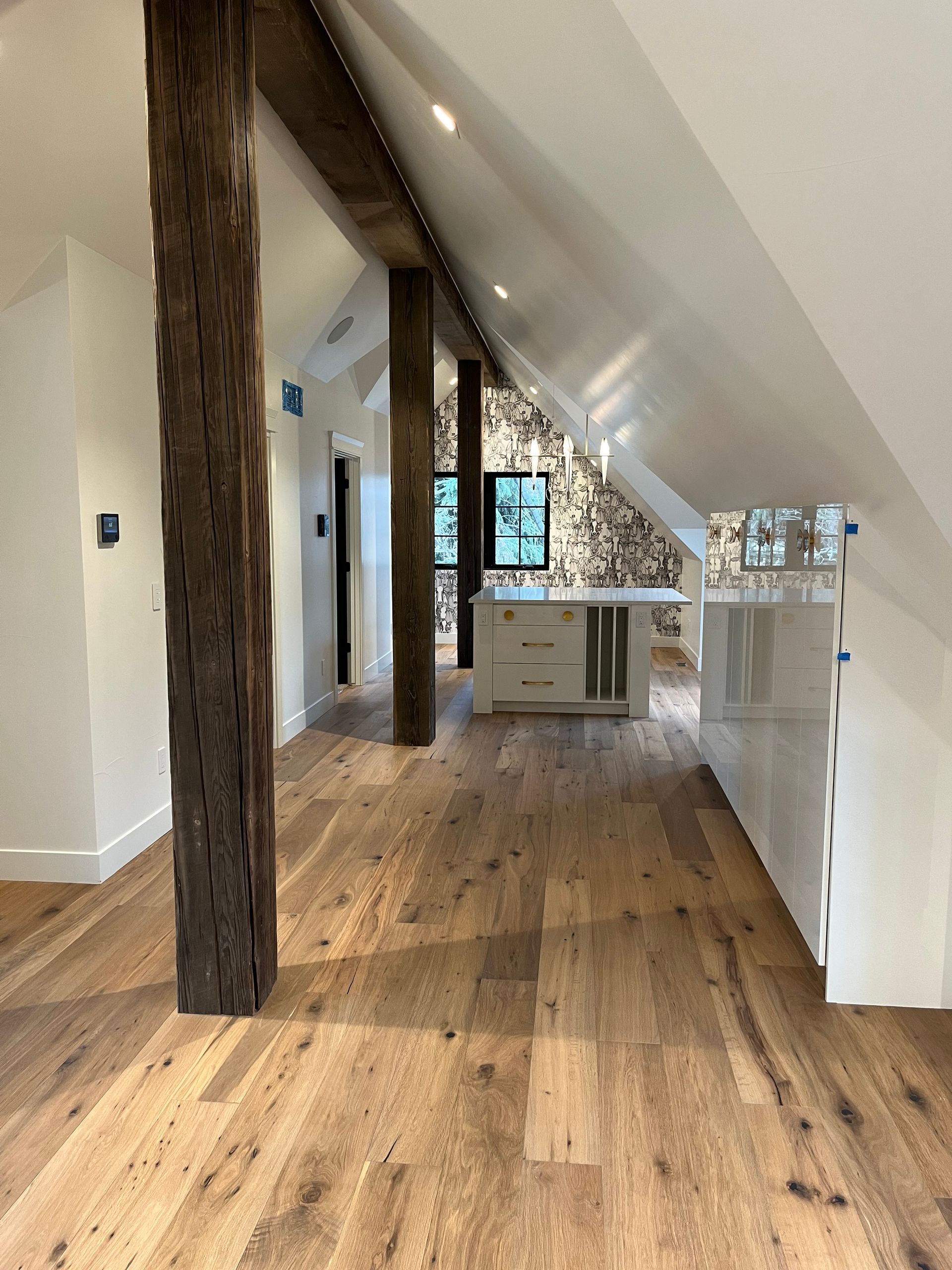 Converted attic with exposed beams, patterned wallpaper, and kitchenette under sloped ceiling