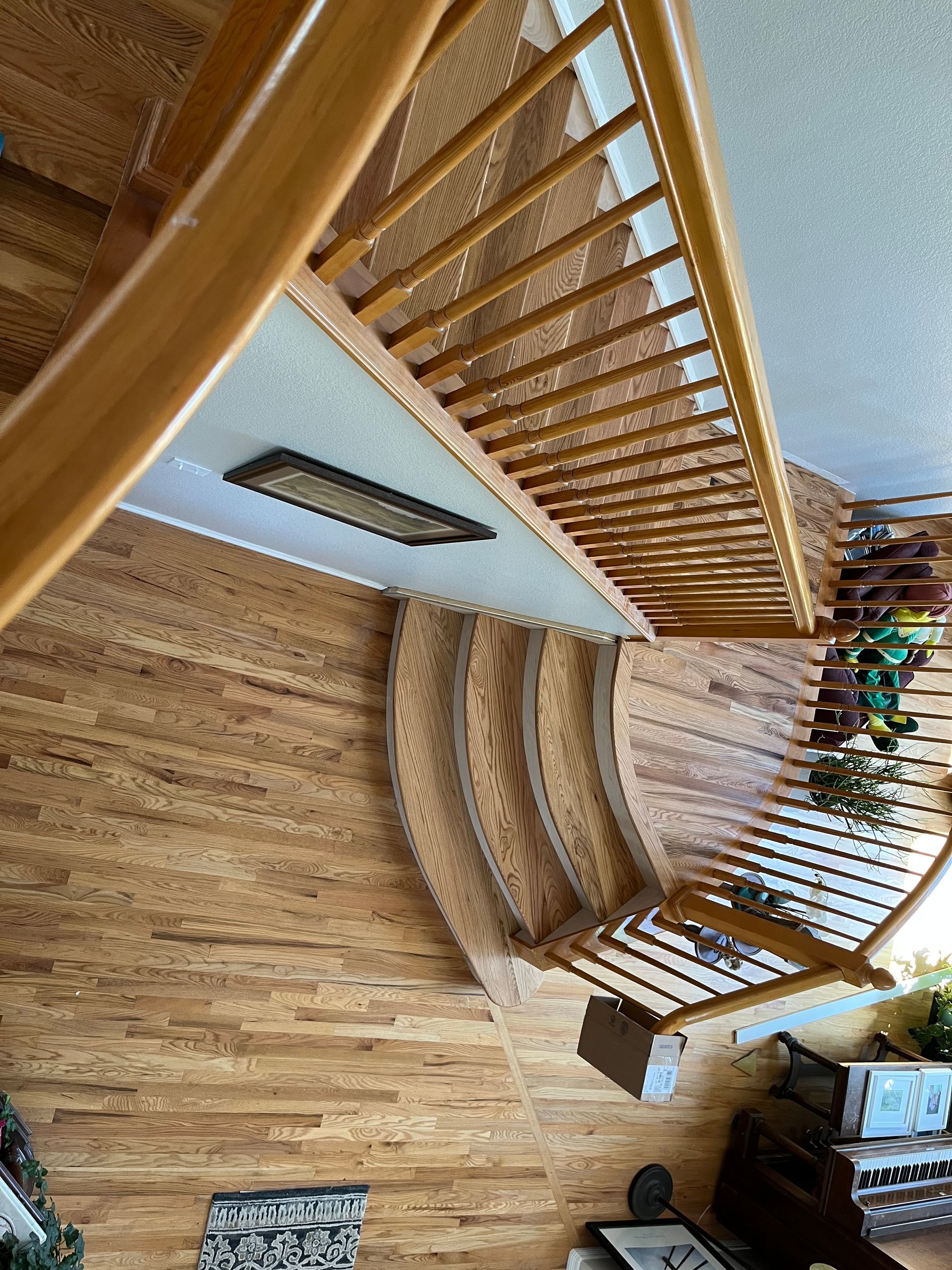 Curved wooden staircase descending to hardwood floor near piano and rug