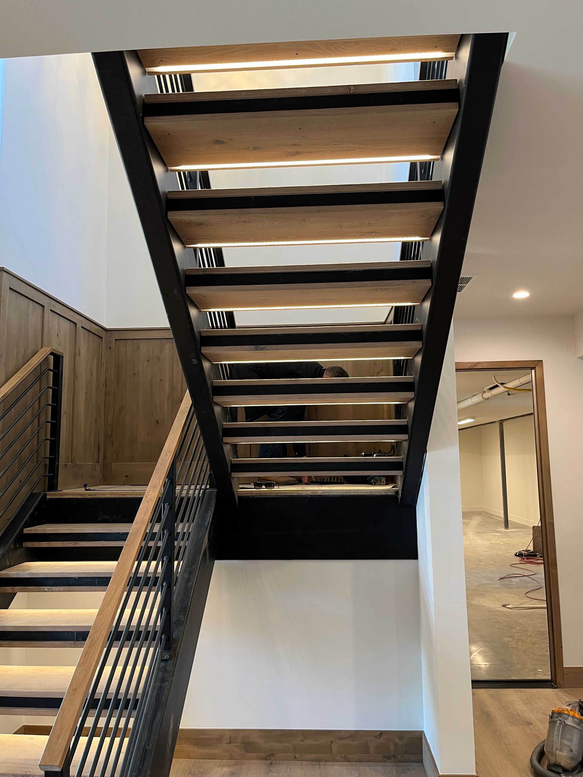 Open-riser staircase with wood treads and black metal railings mid-installation