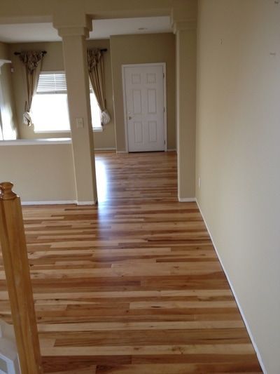 Residential hallway with mixed-tone hardwood floors, columns, and natural light from curtained windows