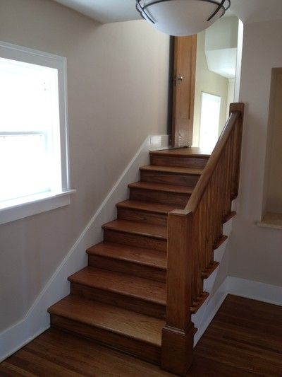 Wood staircase with beige walls, white window trim, and closed door at top landing