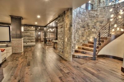 Curved staircase in basement with stone walls, dark wood floors, and bar area in background