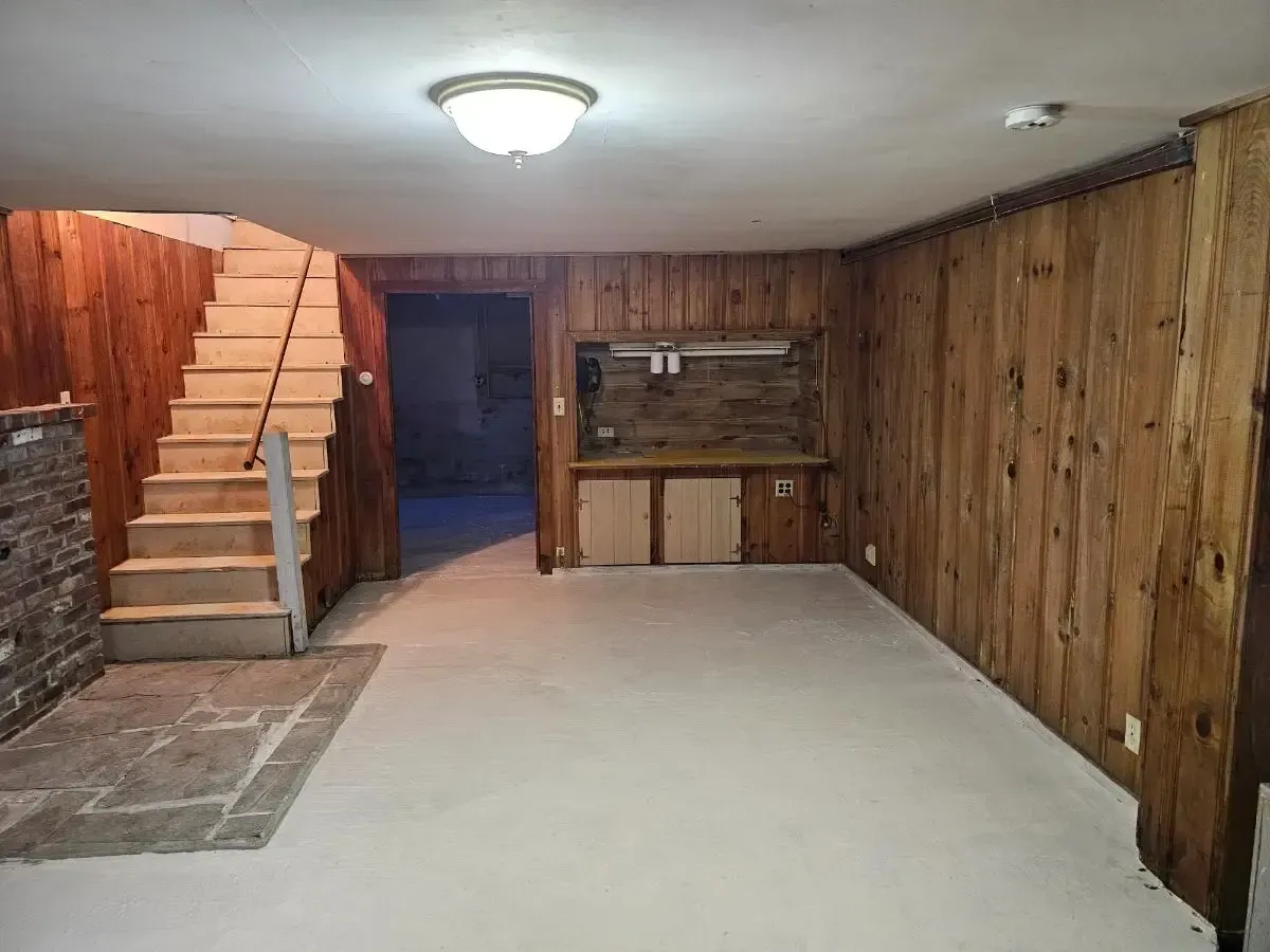 Empty basement with wood paneling, stairs, and a built-in counter area.