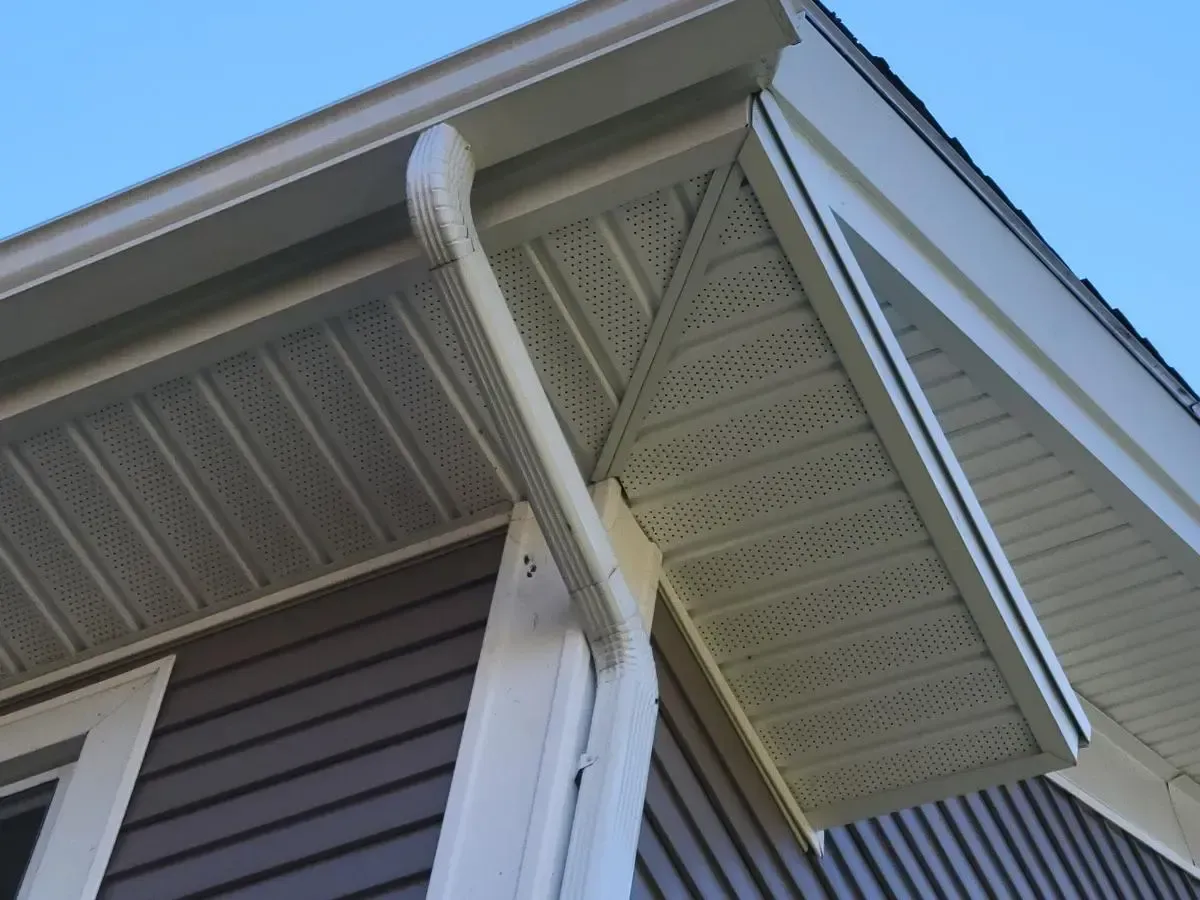 Beige gutters and soffit on a house with brown siding and a blue sky in the background.