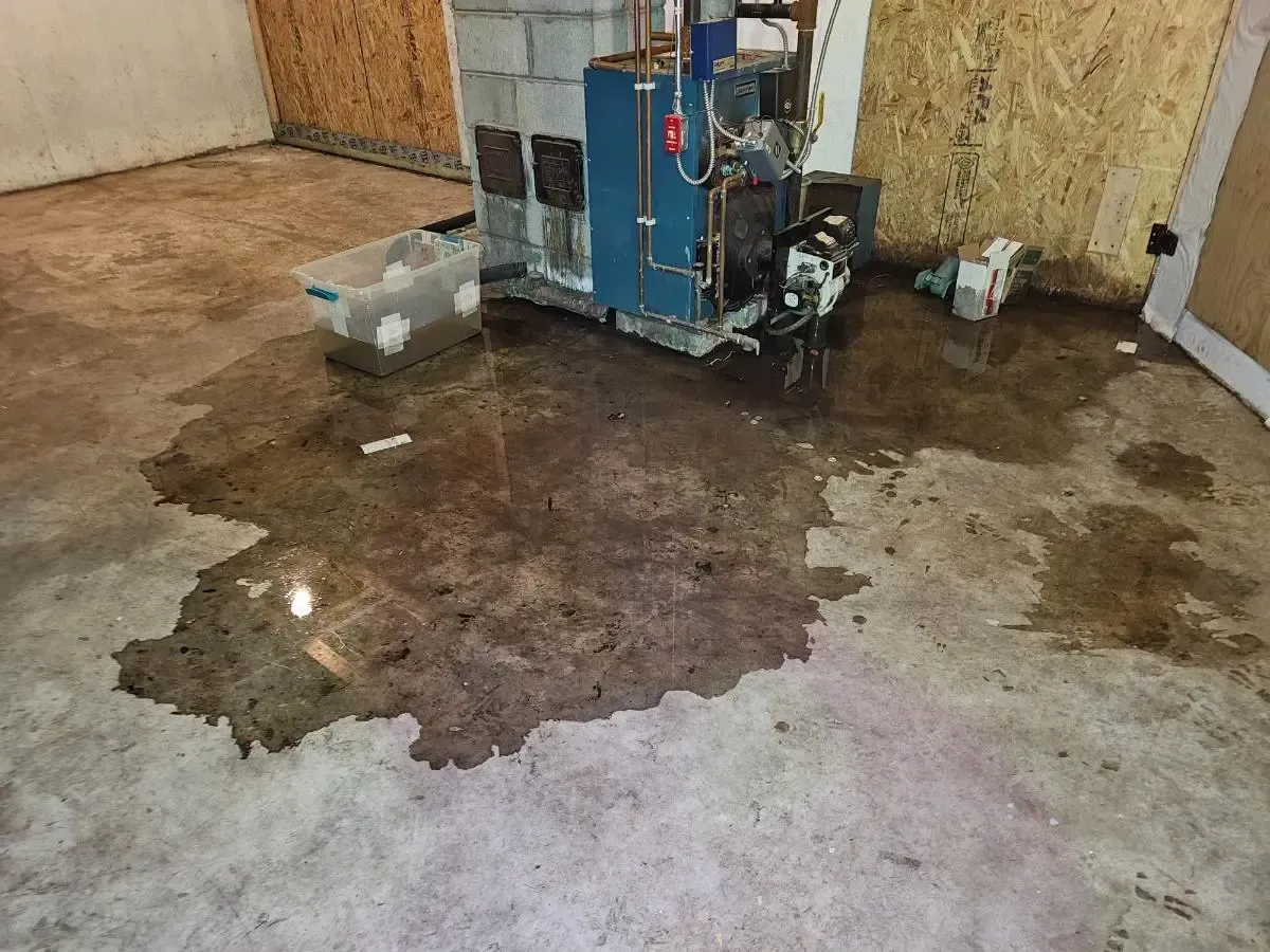 Basement floor flooded; water surrounds heating system and plastic bin, plywood walls.
