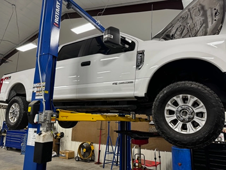 A white truck is sitting on a lift in a garage - Patterson Custom Diesel/Automotive