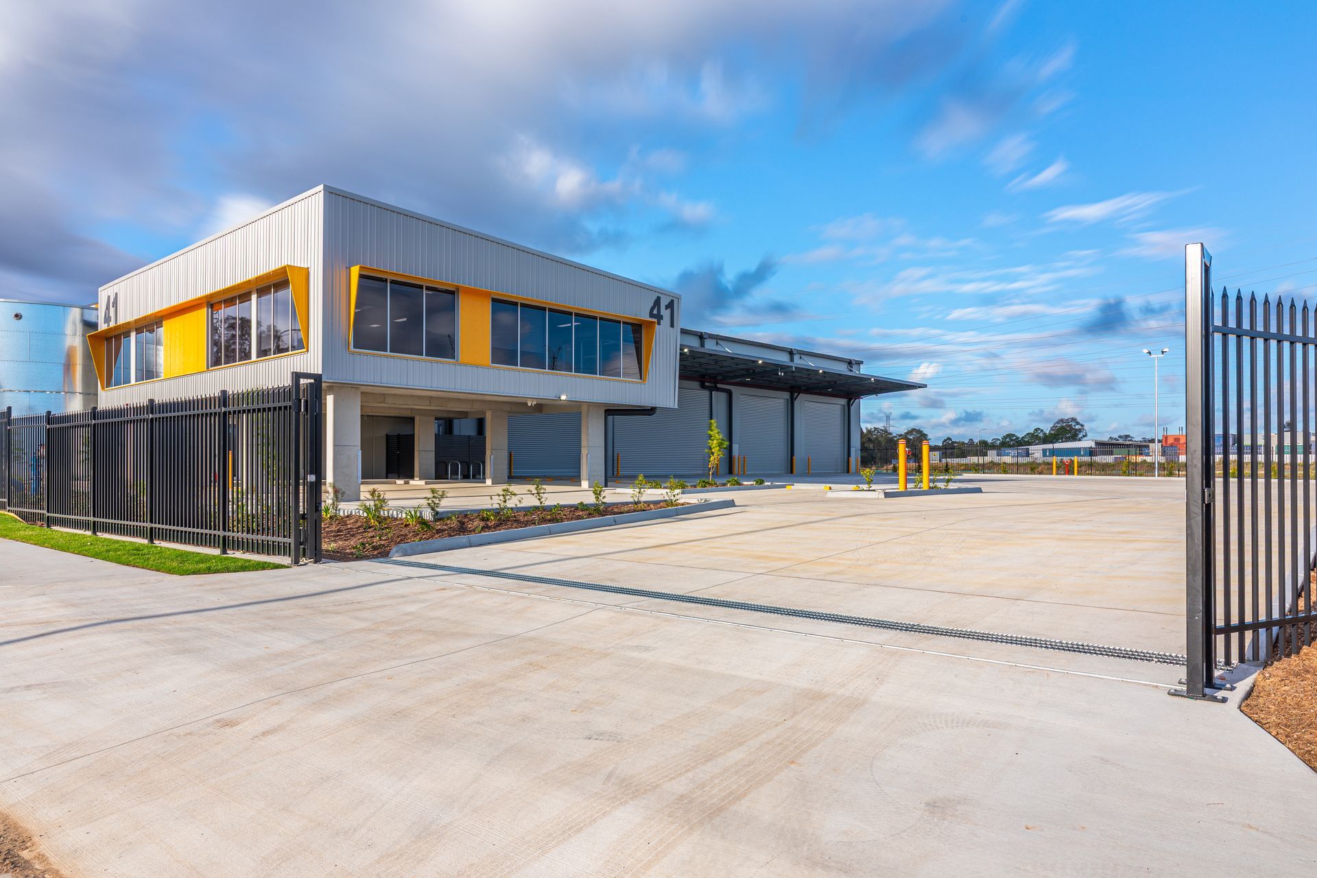 Modern industrial office building with a gated entrance, concrete driveway, and blue sky