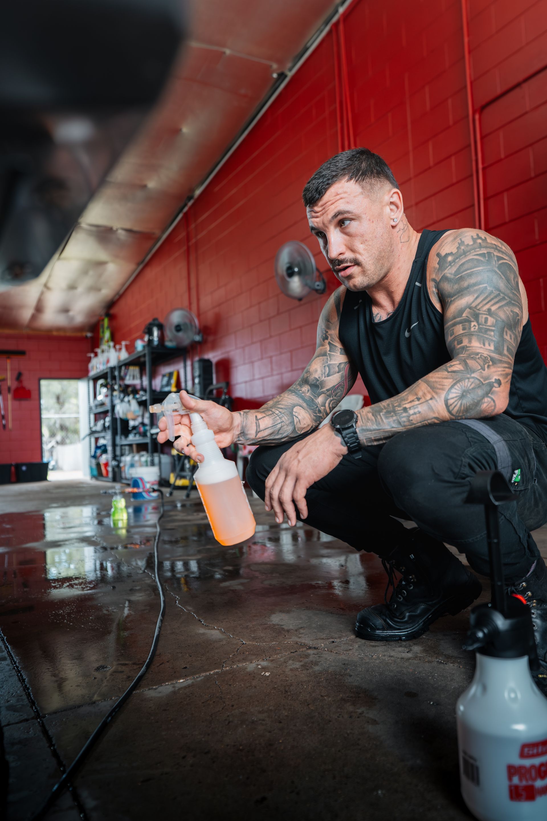 Man With Tattoos Crouching, Holding Spray Bottle in Auto Shop — Mobile Club Cars Cairns in Earlville, QLD