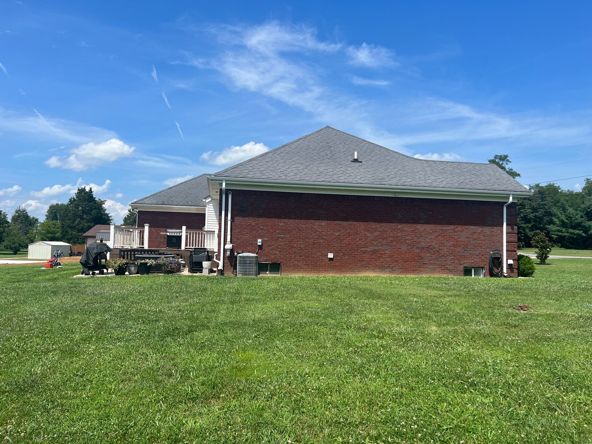 Brick house with a gray roof and a grassy lawn under a blue sky.