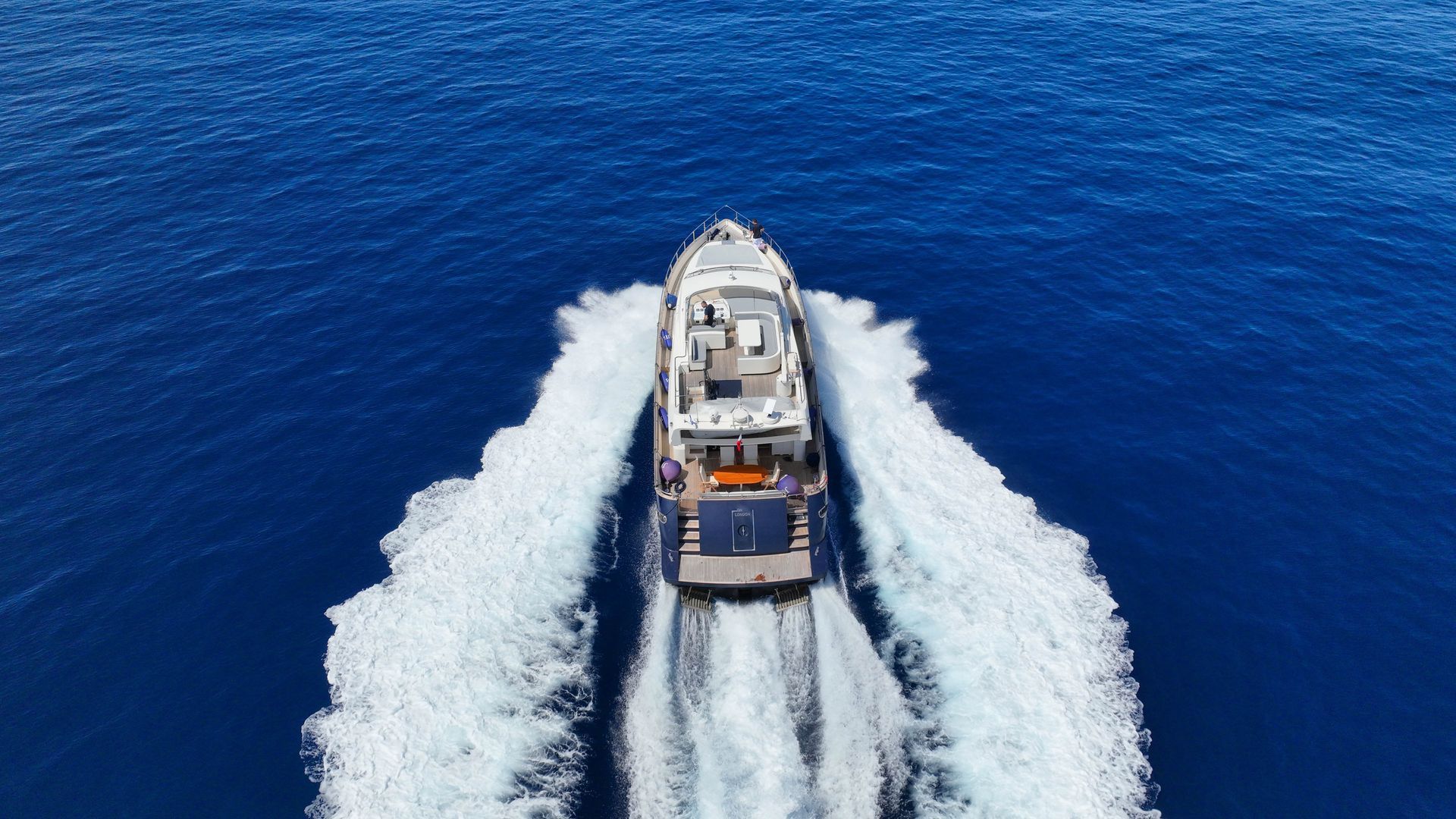 A motor yacht speeding through blue water, leaving white wakes.