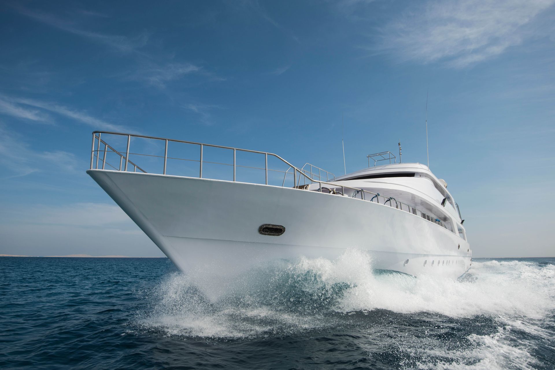 White motor yacht speeding across blue ocean under a clear sky.