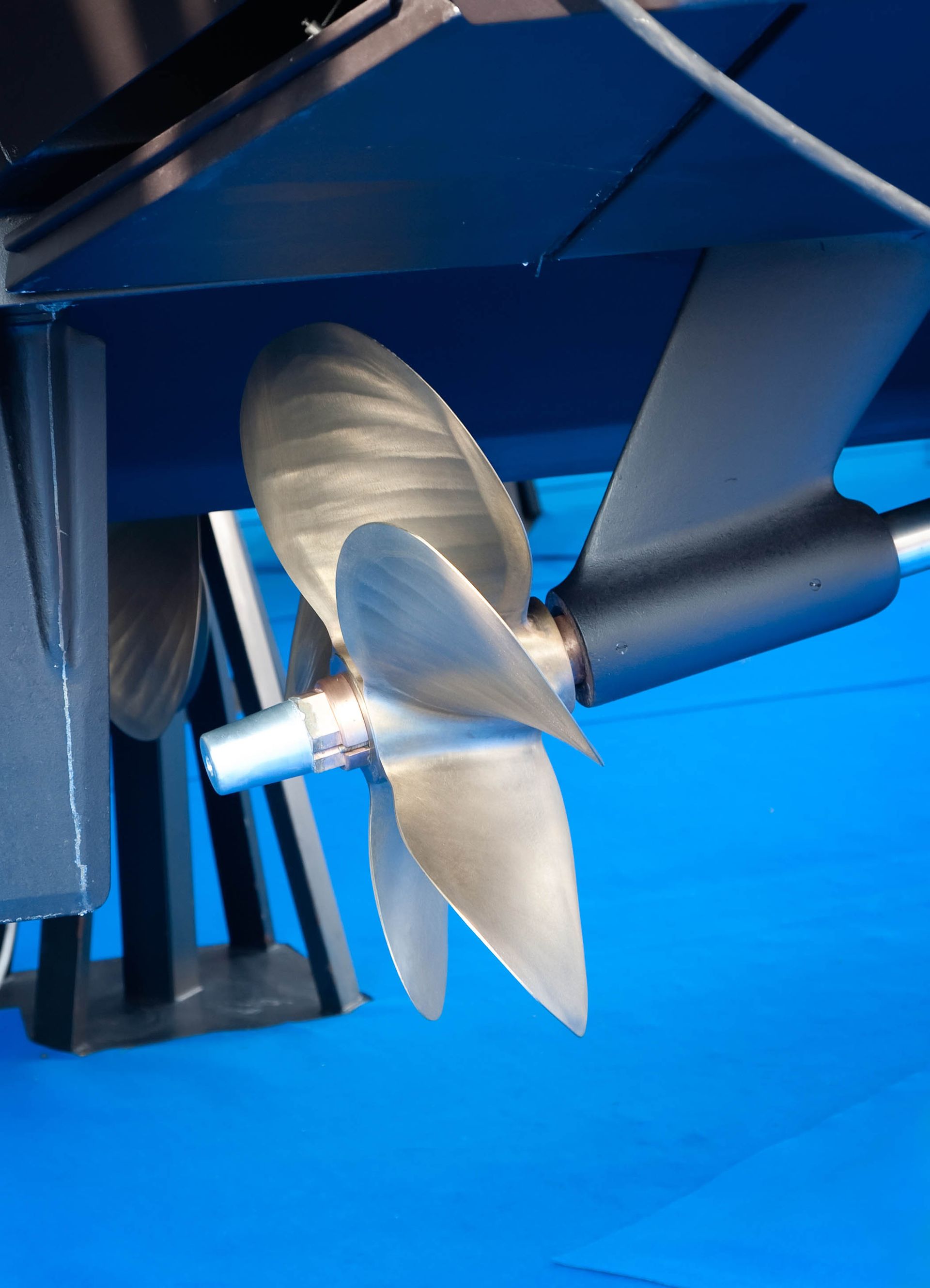 Boat propeller, silver and black, against a blue hull.