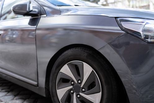Close-up of a gray car’s front side and wheel parked outdoors