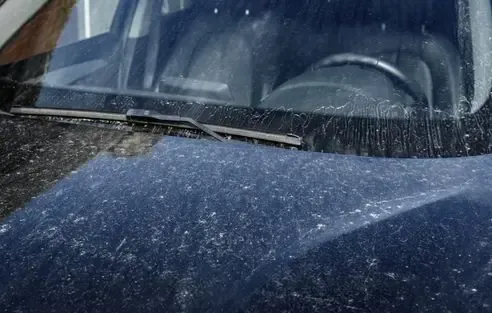 Close-up of a dusty dark car hood and windshield with a wiper at the base