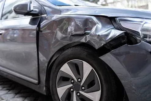 Damaged silver car with crumpled front fender and hood after a collision