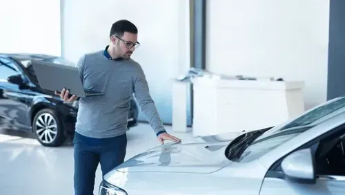 Man inspecting a white car in a bright showroom, with another car in the background