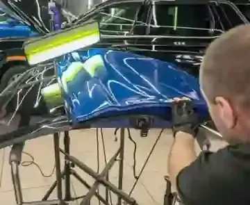 Mechanic applying blue graphics to a car hood in a workshop