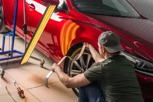 Mechanic applying a vinyl wrap to a red car in a workshop