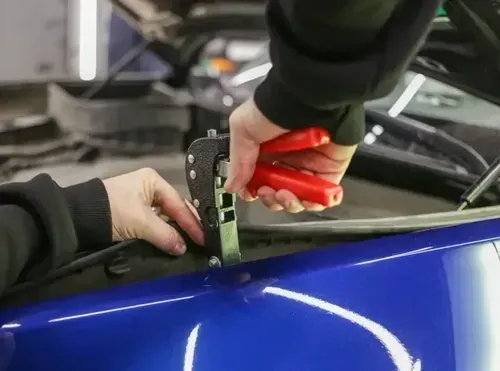 Hands using a tool to apply vinyl wrap to a blue car panel