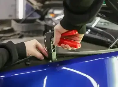 Hands applying red tape to the edge of a blue car window frame
