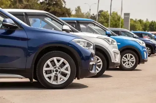Row of parked cars in a lot, including blue, silver, and white vehicles.