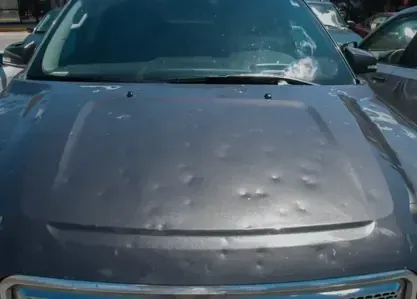 Car hood with multiple hail dents in a parking lot