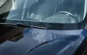 Blue car windshield with visible wiper and reflections of nearby buildings