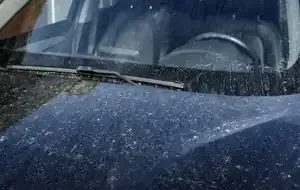 Rain-speckled blue car windshield with wipers visible and driver seat inside