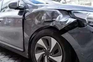 Damaged silver car with a crumpled front-left fender and dented hood after a collision
