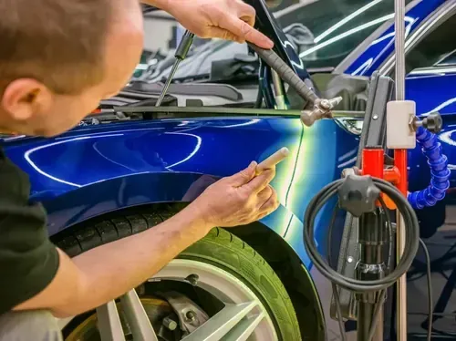 Mechanic sanding a blue car fender in an auto body shop