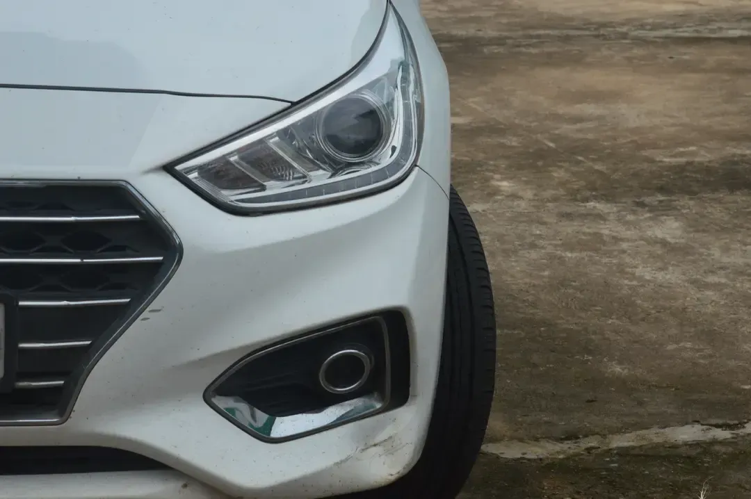 Front-left corner of a white car parked on pavement, showing the headlight and grille