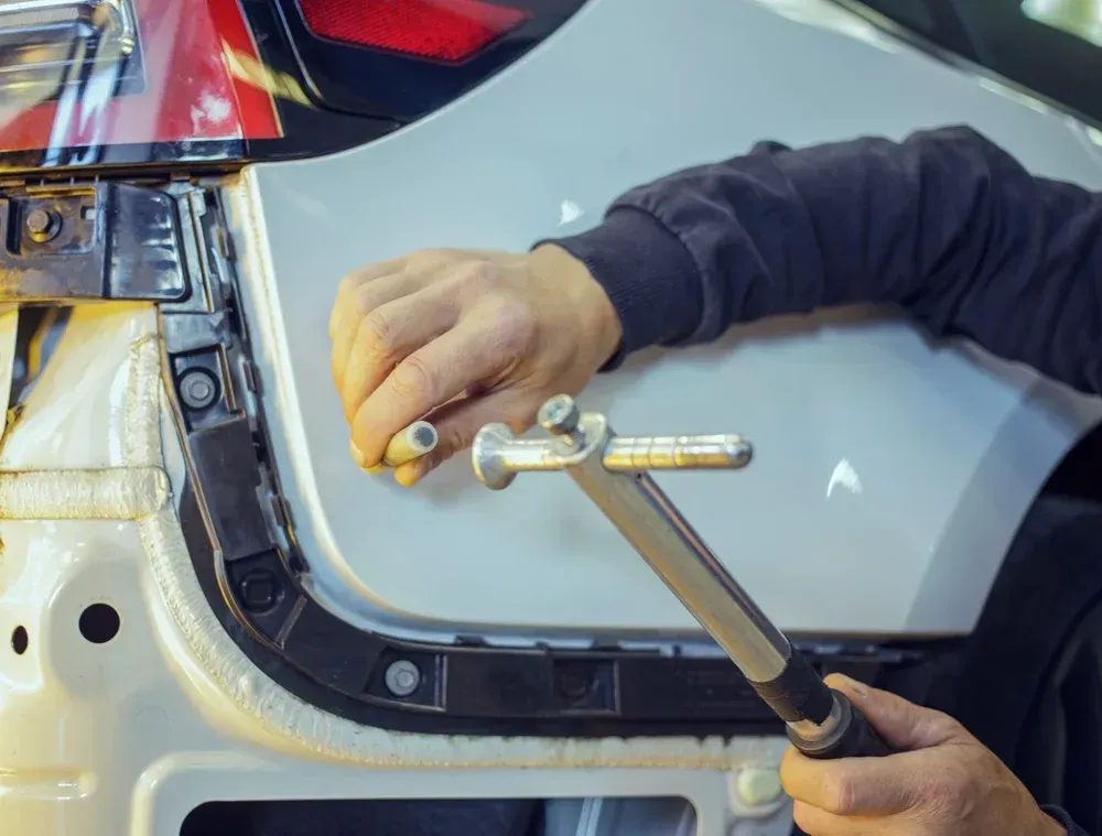 Hands using a hammer and wrench to repair a car body panel near the taillight