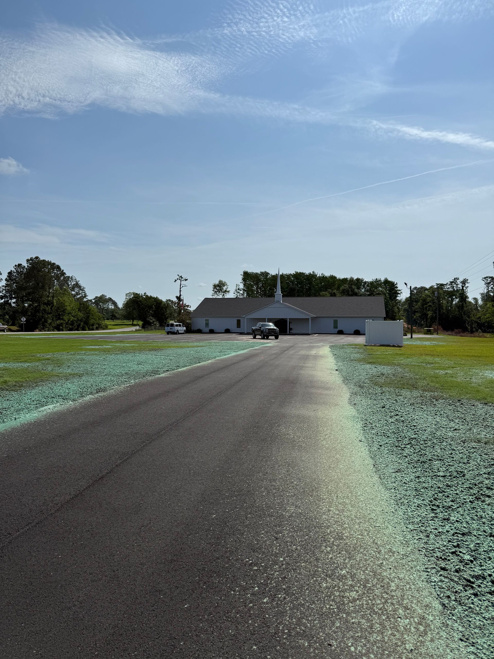Long driveway leading to a white house under a blue sky, with green fields on both sides.