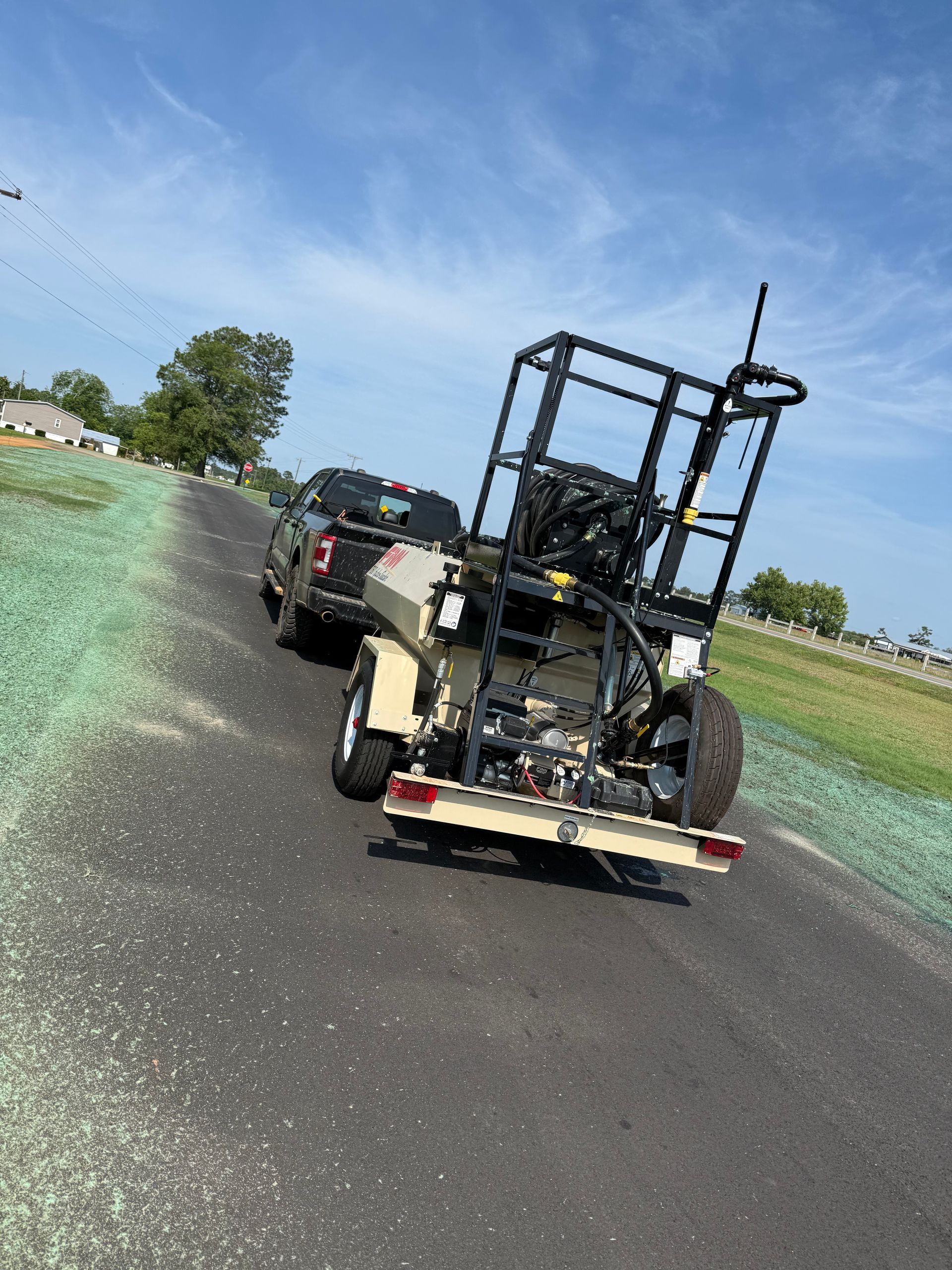 Trailer loaded with roadwork equipment on a rural roadside beside cars under a blue sky