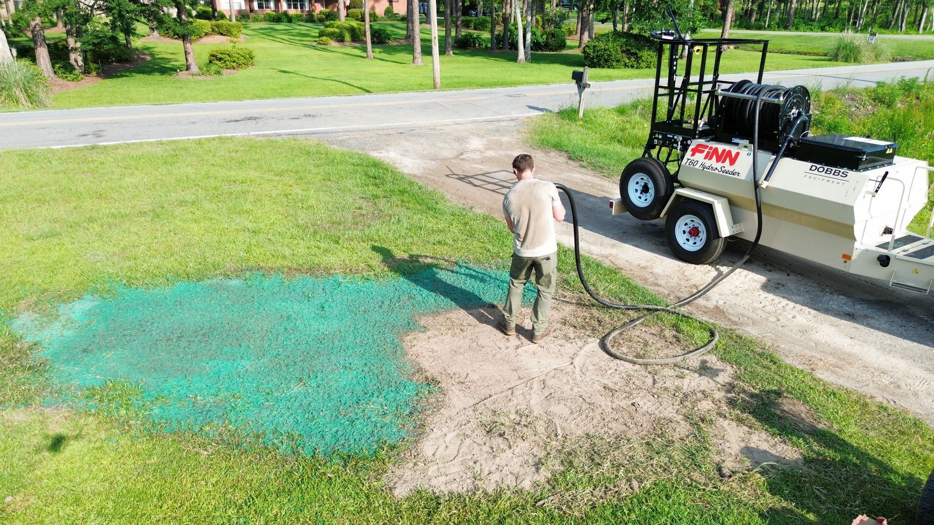 Man spreading green powder on a patchy lawn beside a utility vehicle on a driveway