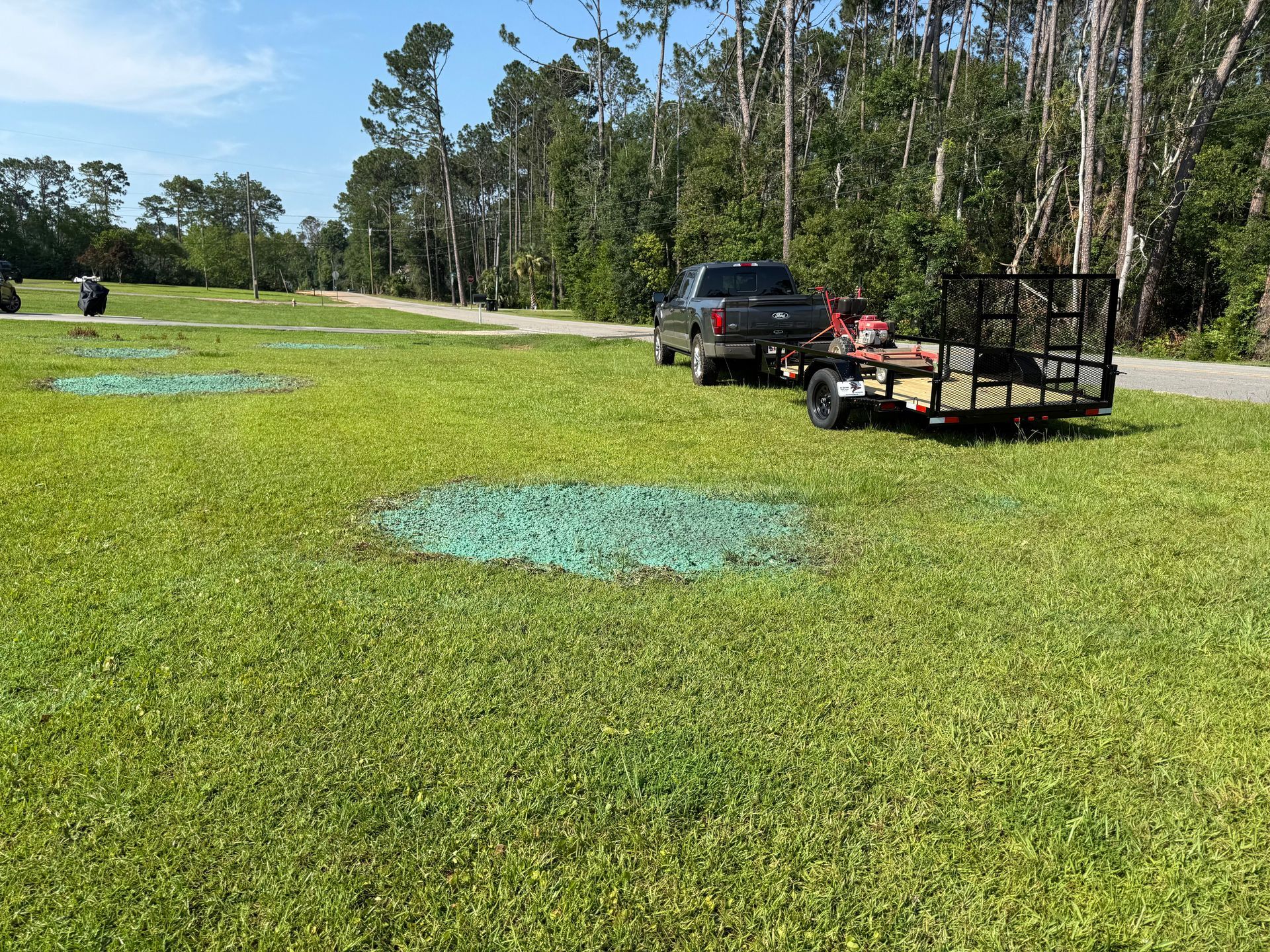 Lawn with blue spray markings, a black SUV, and a trailer in a grassy field near trees