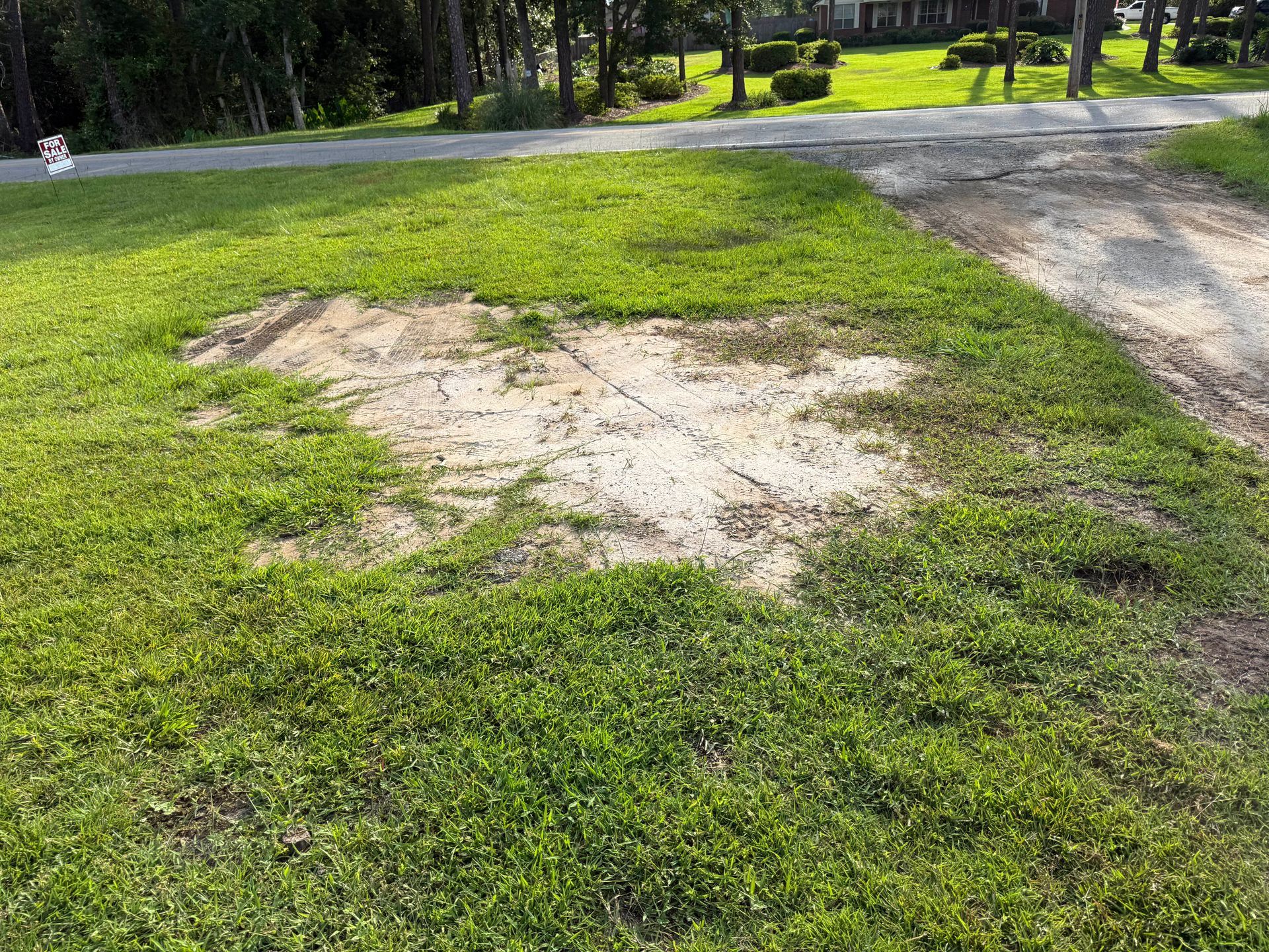 Bare dirt patch in a grassy park near a gravel path and trees