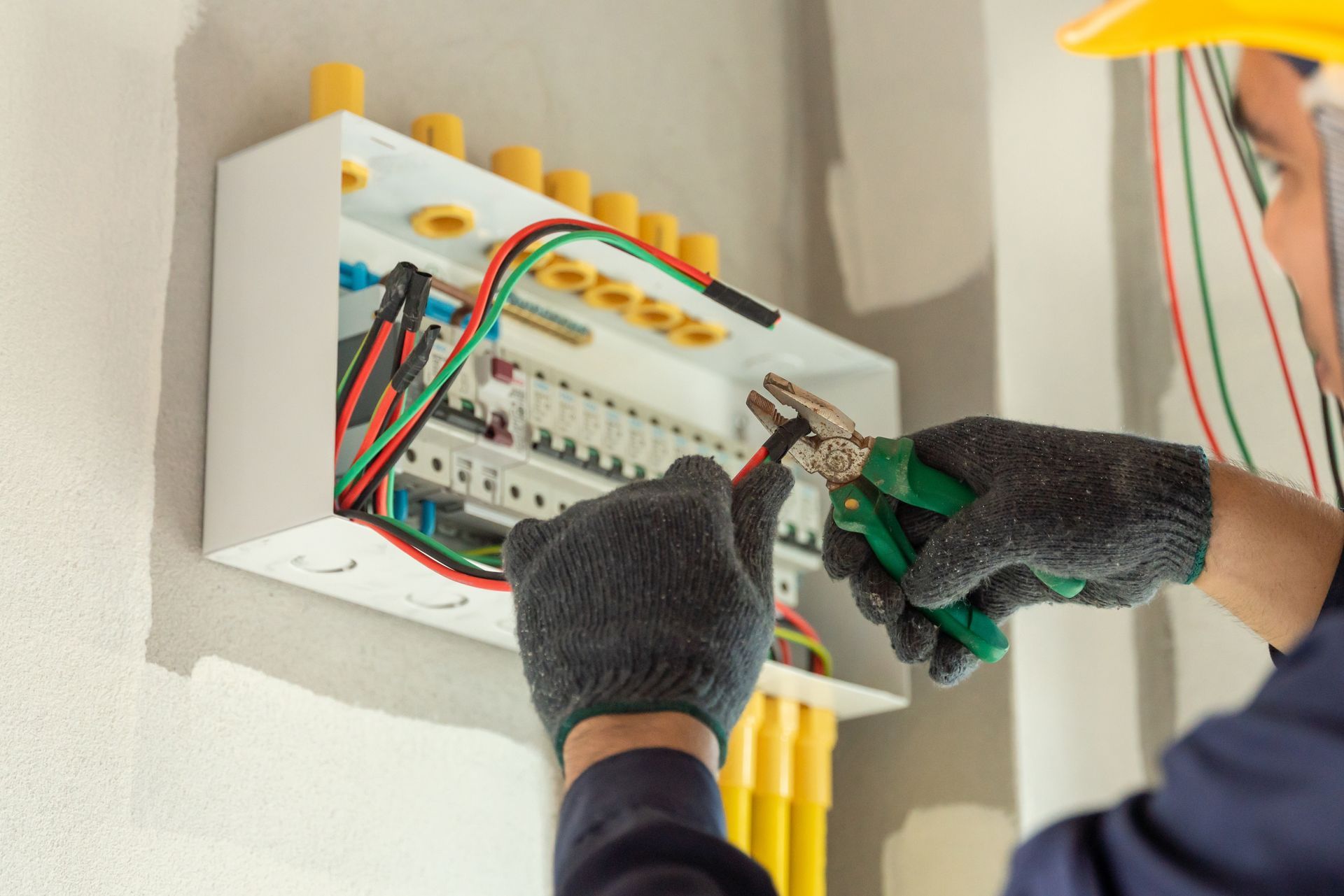 Gloved hands wiring an electrical circuit breaker panel with colorful cables.