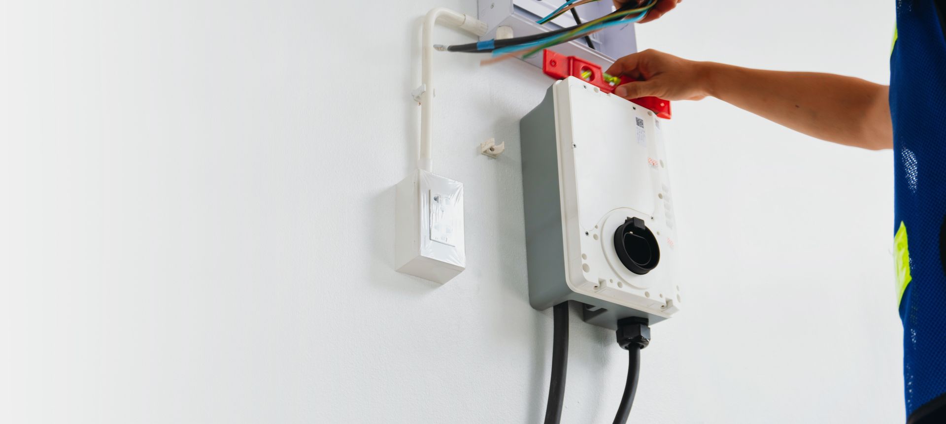 Technician testing a wall-mounted electrical device with a multimeter in a white room