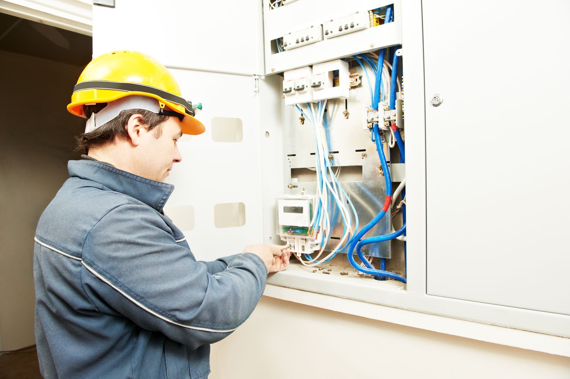 Technician in hard hat inspecting an open electrical control panel with blue wiring and equipment.