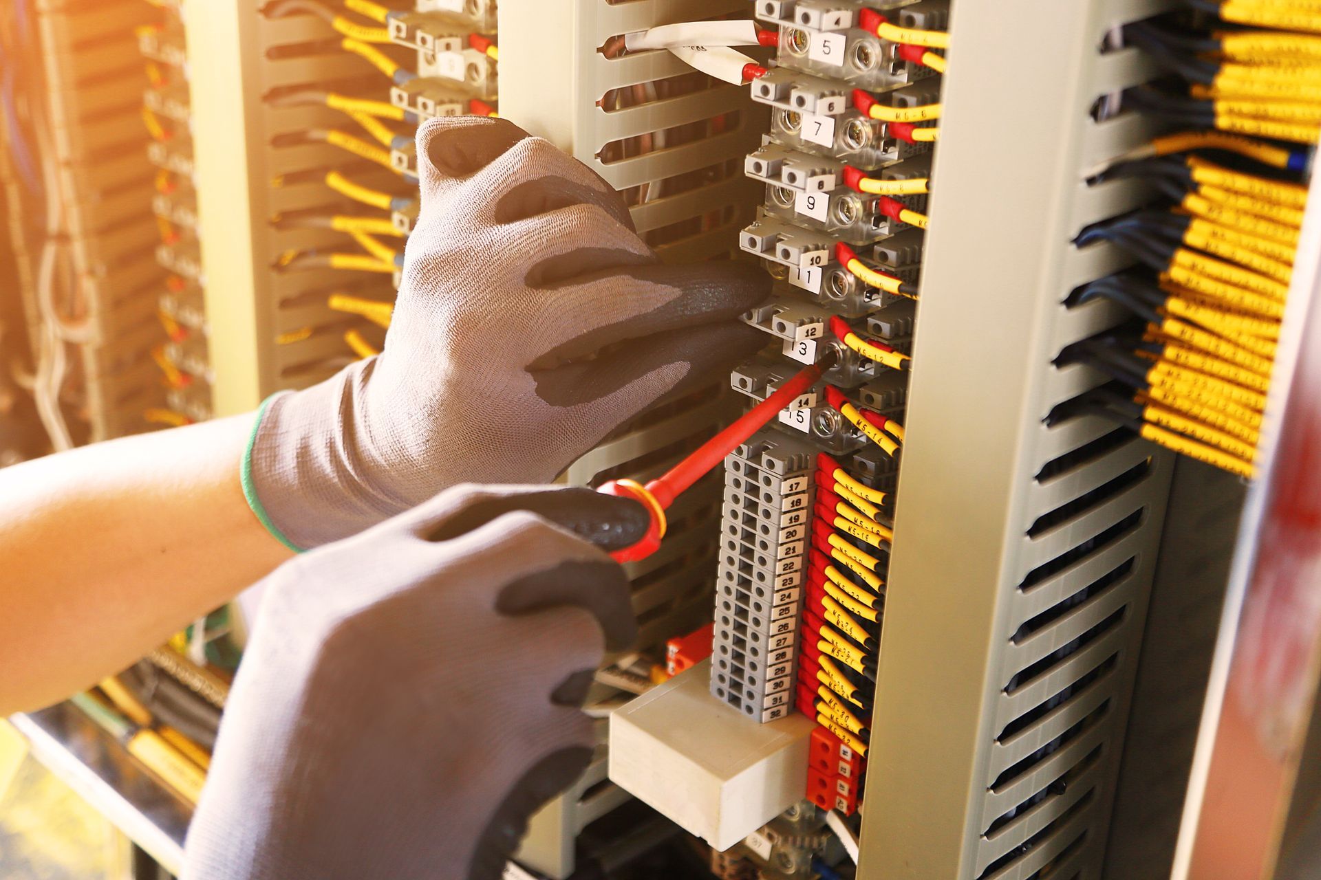 Gloved hands wiring an electrical panel with red and black cables and labeled breakers