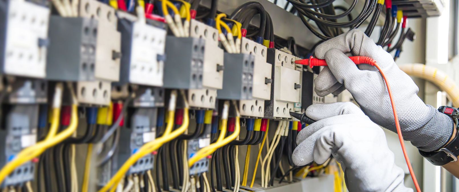 Gloved hands wiring electrical control panels with colored cables in an industrial setting